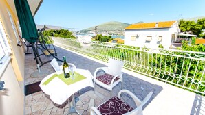 A balcony with a table and chairs, a bottle of wine, and a view of a town and hills. - Apartments Ivana - Studio With Balcony and Sea View (Trogir)