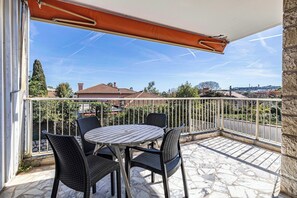 Ein Balkon mit Tisch und Stühlen, Blick auf Häuser und einem klaren Himmel.