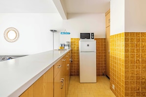 Een kleine keuken met een koelkast, magnetron en koffiezetapparaat op het aanrecht.