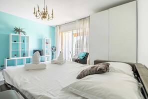 Ein Schlafzimmer mit einem Bett, einem Sessel, einem Schreibtisch, einem Fernseher und einem Fenster mit Vorhängen.