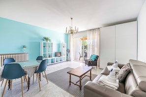 Een moderne woonkamer met een eethoek, een zithoek, een kroonluchter en uitzicht door een raam.