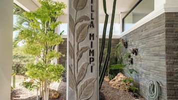 A stone pillar with the inscription 'VILLA MIMPI' in a courtyard with plants and a stone wall.