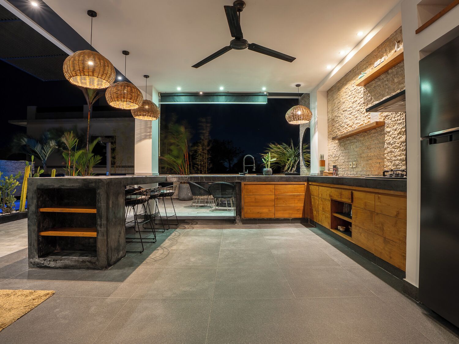 An outdoor kitchen area with a dining set, a ceiling fan, and hanging lights.
