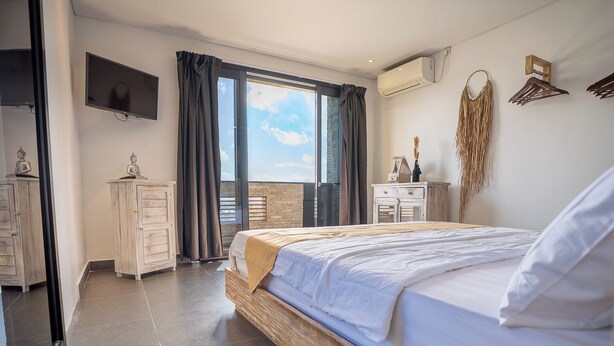 Ein Schlafzimmer mit einem Bett, einem Schminktischchen, einem Fernseher und einem Balkon mit Blick.