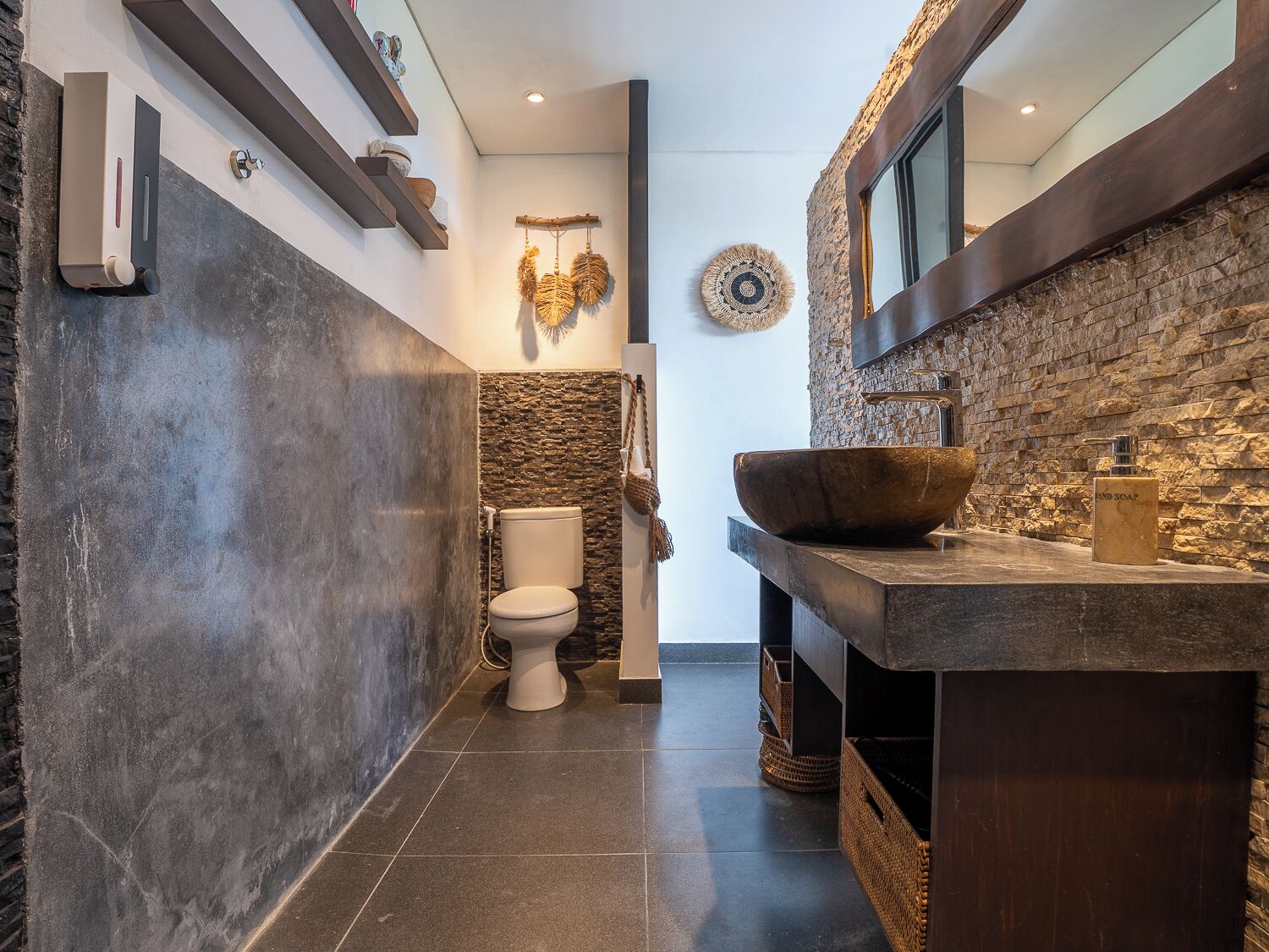 A modern bathroom with a stone wall, a large wooden basin, and a toilet.