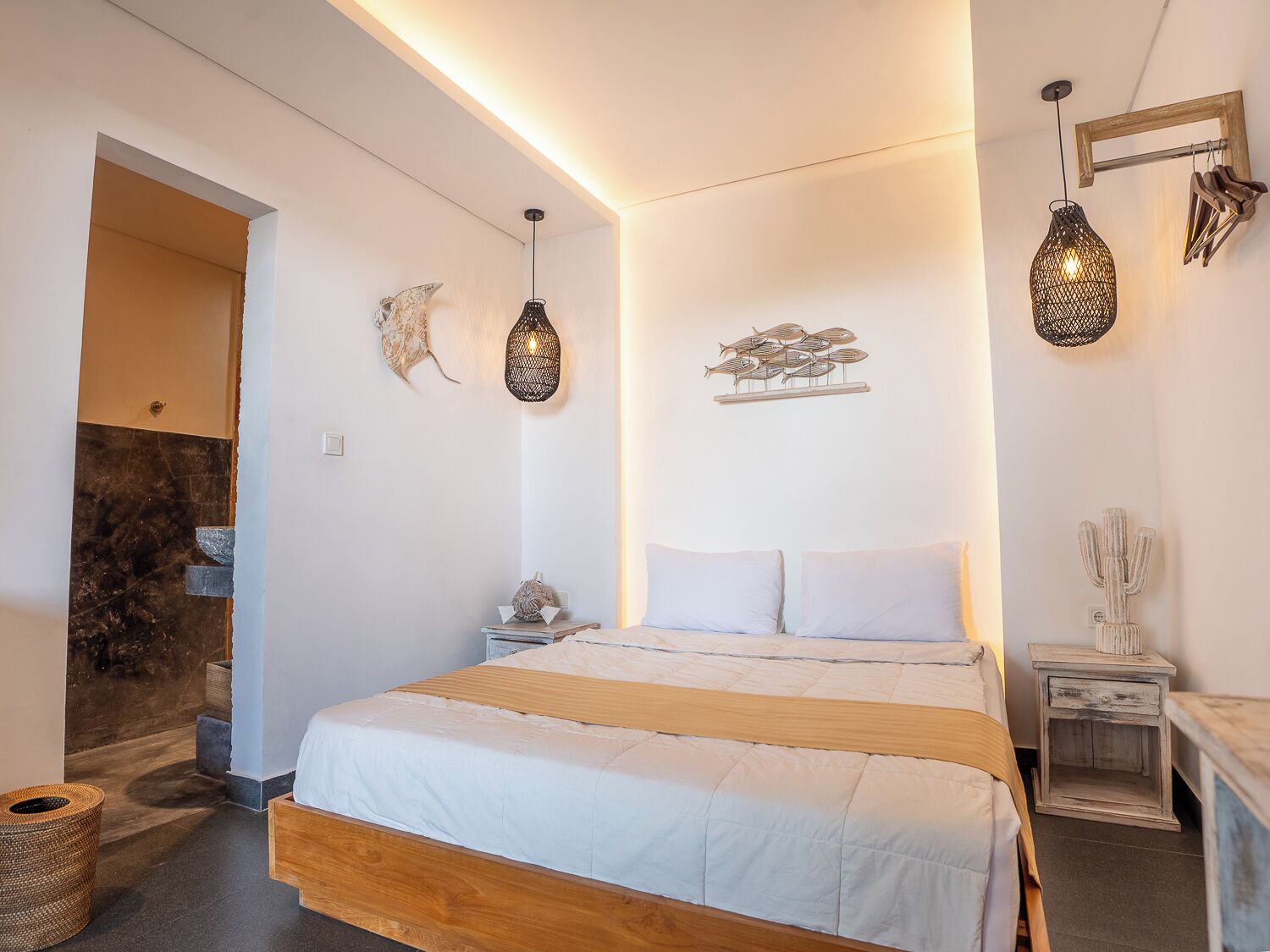 A bedroom with a wooden bed, white bedding, a nightstand with a lamp, and wall art including a fish sculpture and a cactus.