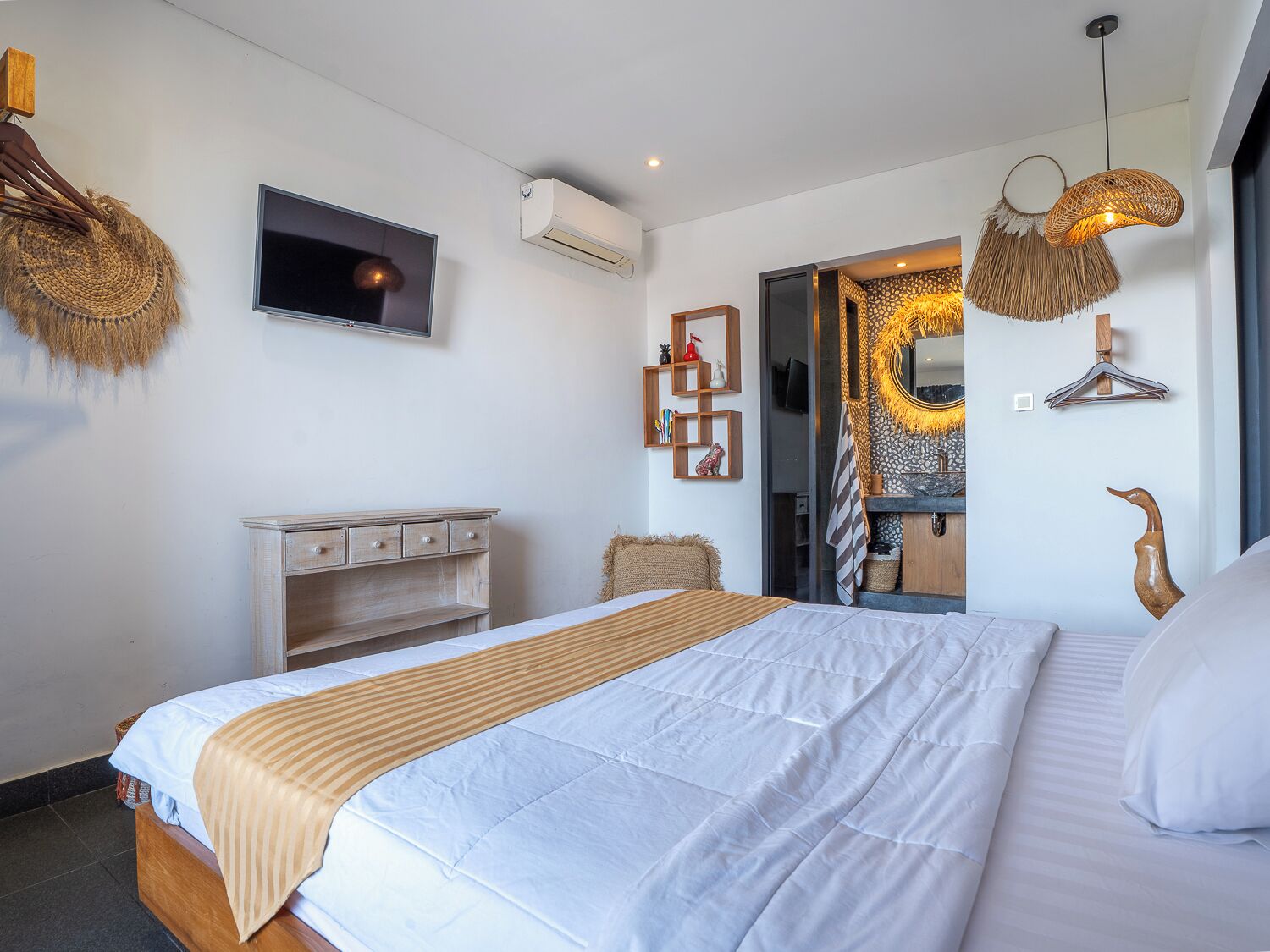 Un dormitorio moderno con una cama grande, un televisor, un armario y un baño visible a través de una puerta abierta.