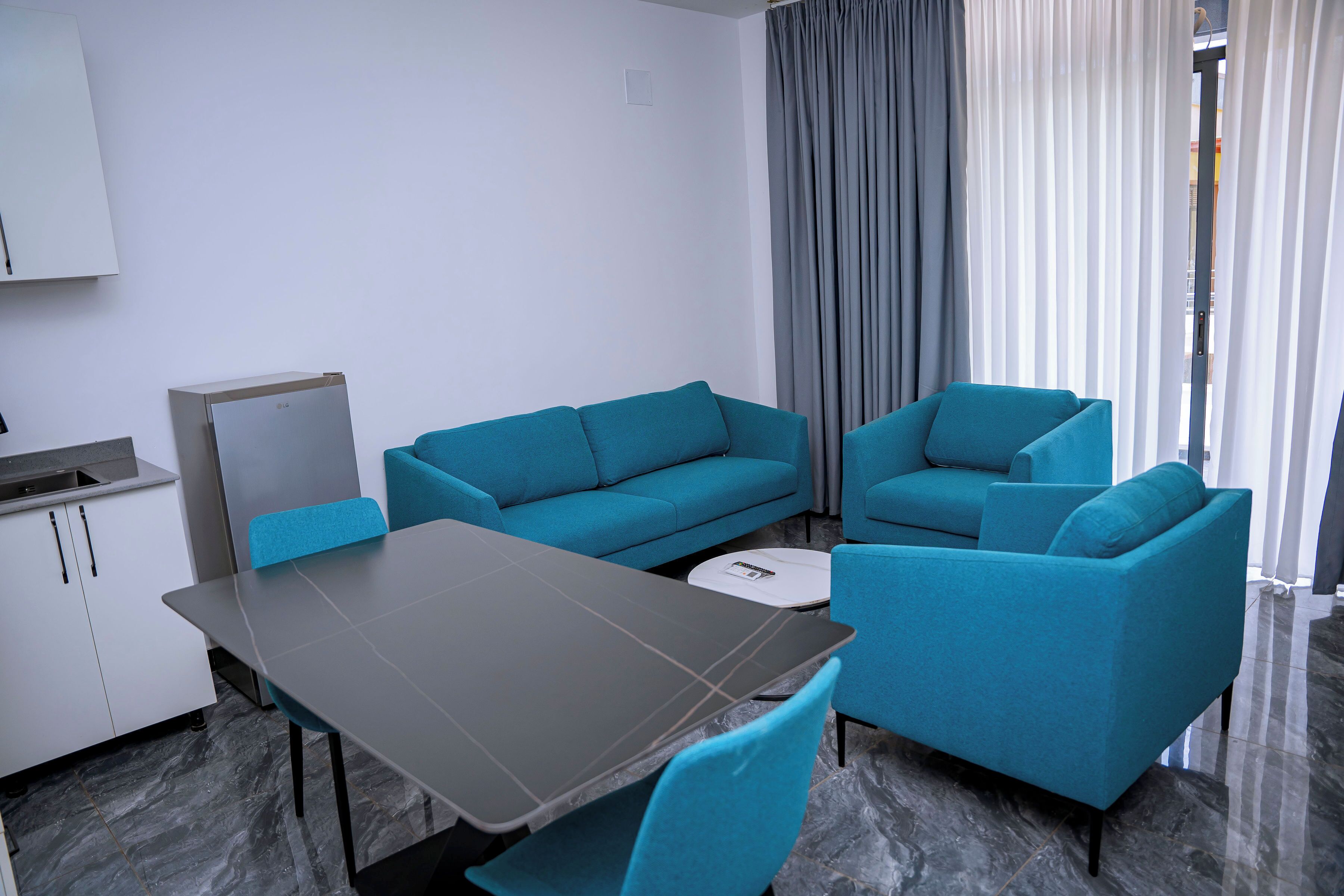 A modern room with a dining table, two sofas, a kitchen area, and a window with curtains.