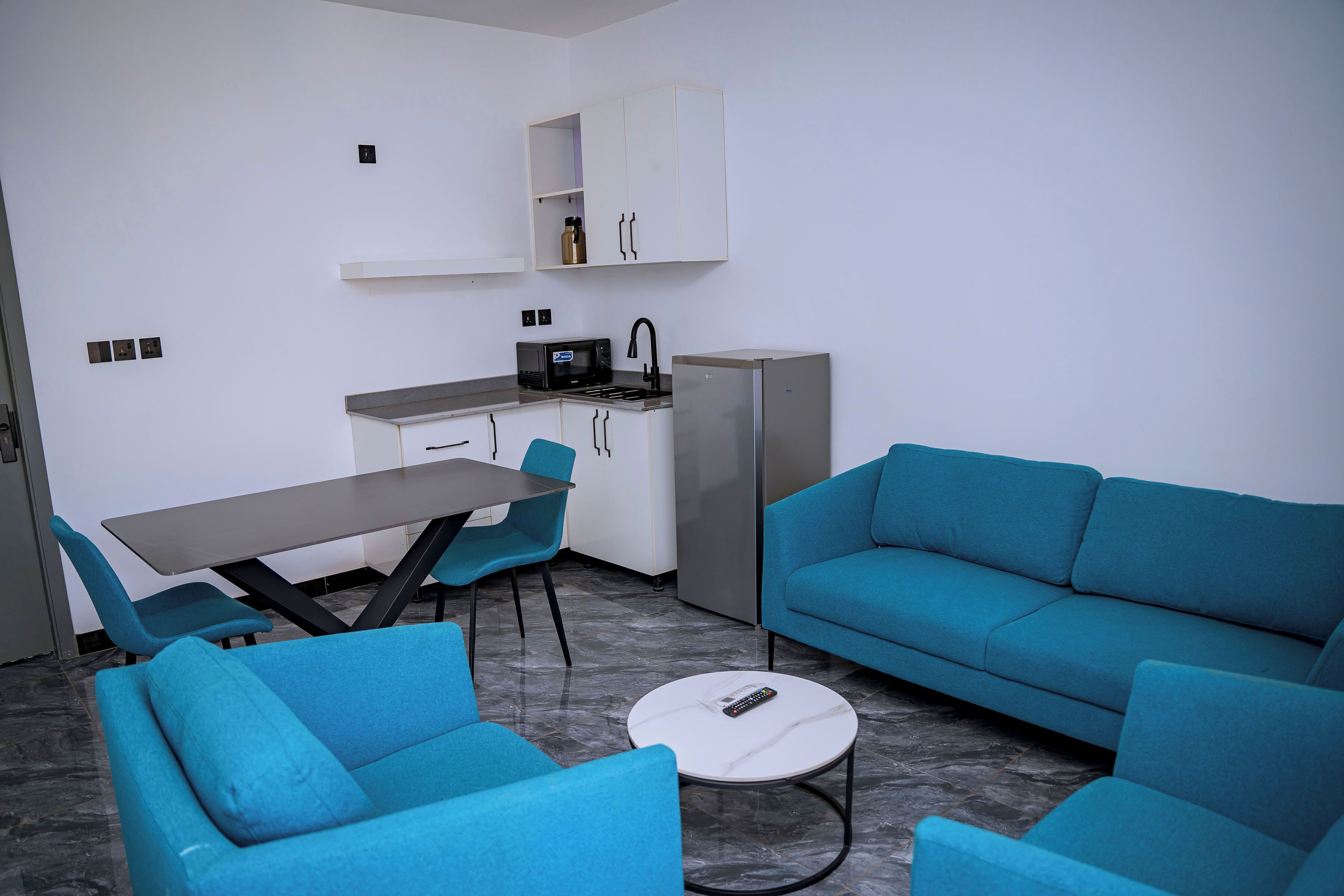 A modern kitchen with a microwave, sink, and refrigerator. There is a dining table with chairs and a sofa.