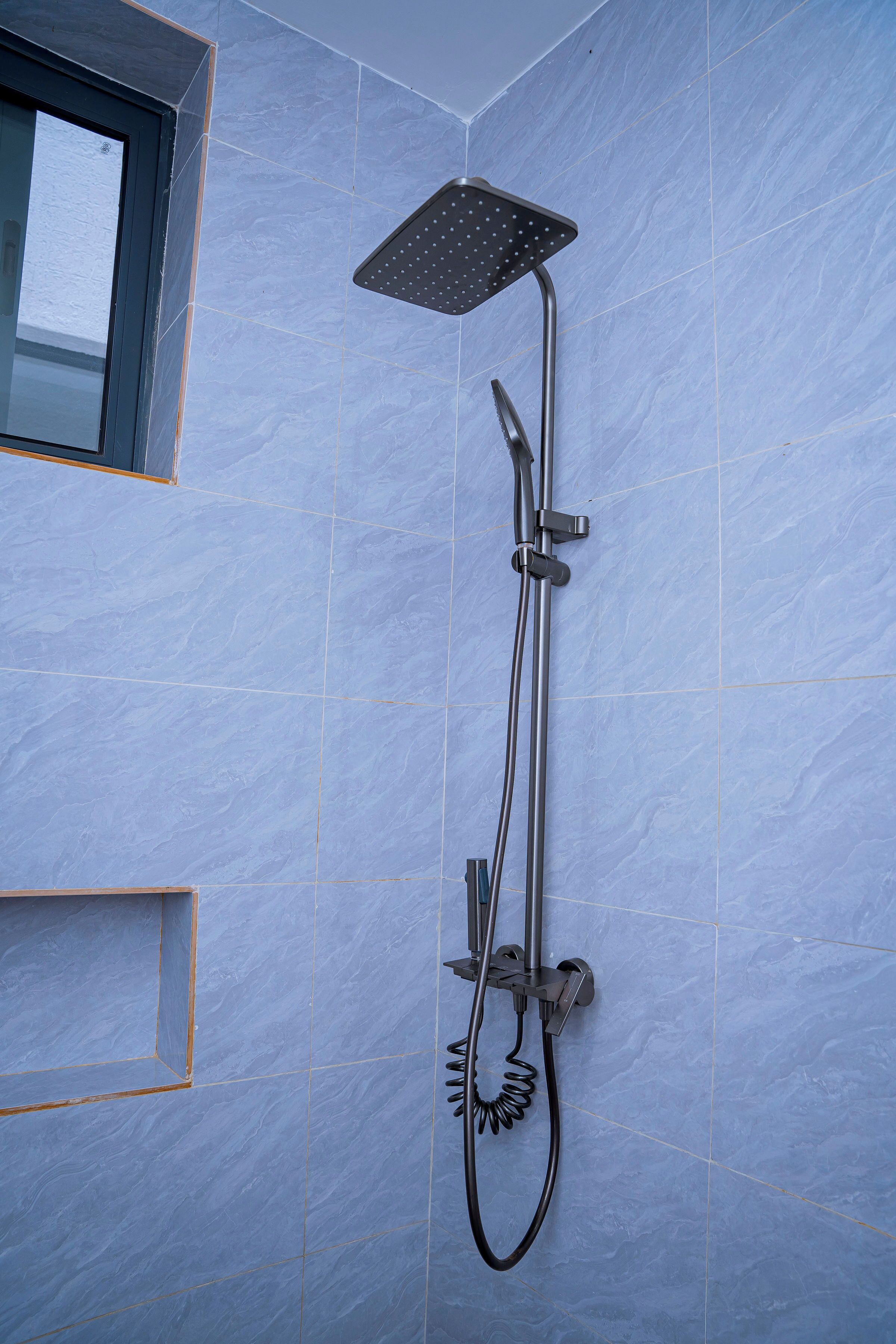 Eine Dusche mit Handbrause und Deckenbrause in einem Badezimmer mit blauen Fliesen.