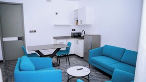 A compact living space with a kitchenette, a dining table, two blue sofas, and a small round table. - Ink & S Apartment Hotel (Kigali)