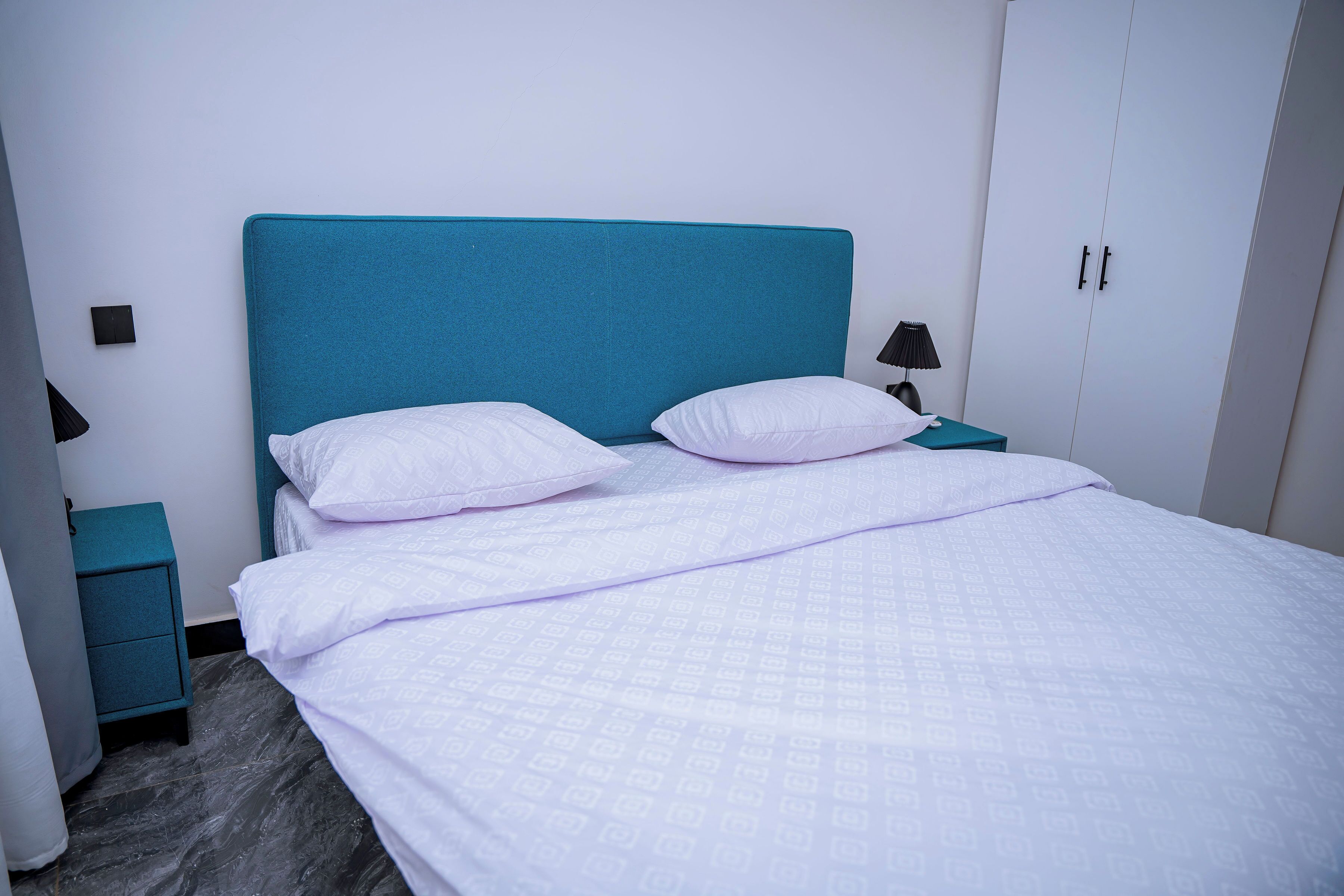 Un lit avec une tête de lit de couleur turquoise, une literie blanche et une table de chevet avec une lampe.
