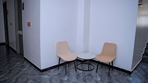 Un vestíbulo de hotel con una recepción, dos sillas, una mesita y un detector de incendios.