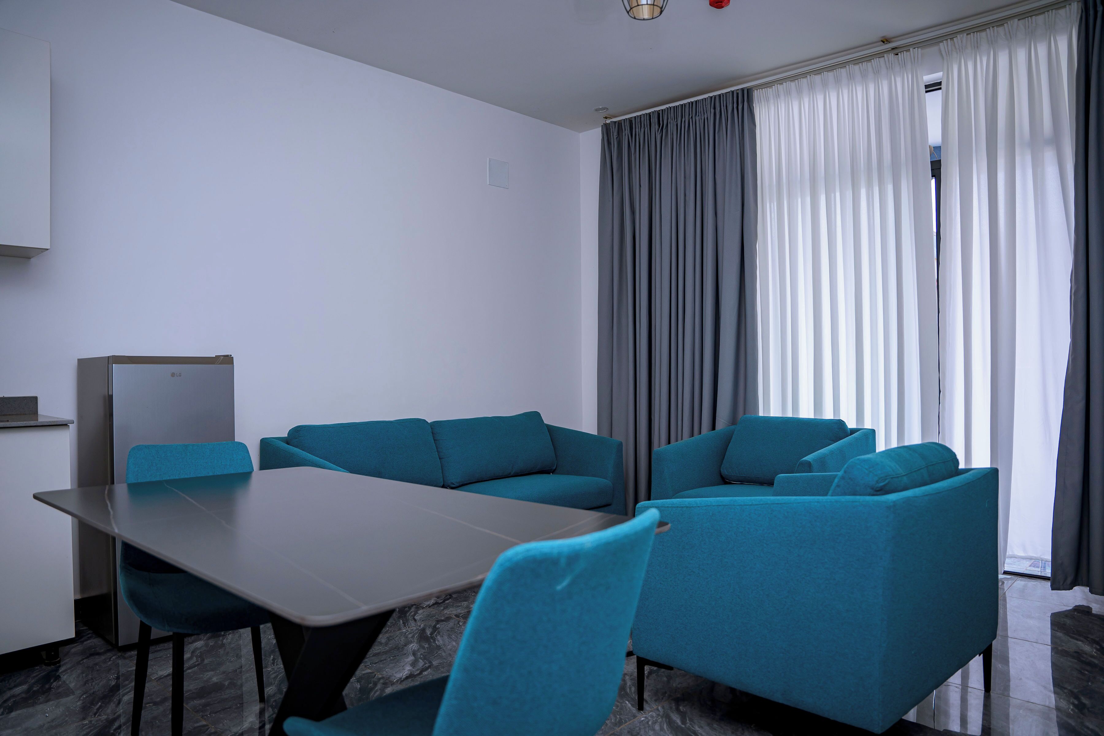 A modern room with a grey table, teal chairs, and a grey sofa.