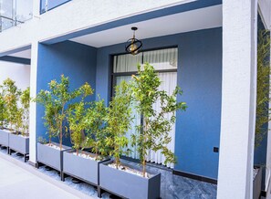 A modern building exterior with a blue facade, multiple planters with greenery, and a window with blinds. - Ink & S Apartment Hotel (Kigali)