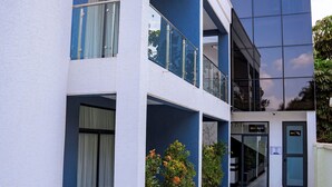 A multi-story building with a white facade, balconies, and a blue glass building adjacent to it. - Ink & S Apartment Hotel (Kigali)
