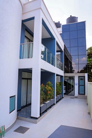 Un edificio de varios pisos con fachada blanca, balcones y un edificio de vidrio azul contiguo.