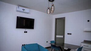 Una habitación moderna con televisión de pantalla plana, una mesa de comedor con sillas, una pequeña kitchenette y aire acondicionado instalado en el techo.