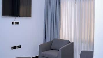 A modern living room with a flat-screen TV, grey sofas, a round coffee table, and a ceiling-mounted air conditioning unit.