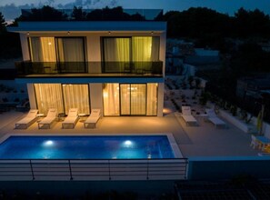 Ein modernes, zweistöckiges Haus mit Schwimmbad, Sitzgelegenheiten im Freien und einem Balkon.