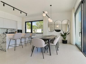 Eine moderne Küche mit weißen Schränken, einer Marmorarbeitsplatte und einem Essbereich mit Tisch und Stühlen.