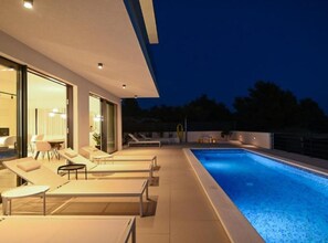 Ein moderner Poolbereich im Freien mit Liegestühlen und einem durch Glas geschützten Raum.