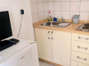 Eine Küche mit Spüle, Arbeitsplatte und Schränken. Auf einem Tisch befinden sich ein Fernseher und Fernbedienungen.