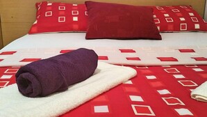 Ein Bett mit einer rot-weißen Bettdecke, einem violetten Handtuch und zwei roten Kissen.
