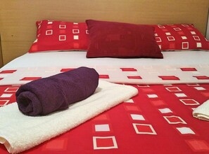 Ein Bett mit einer rot-weißen Bettdecke, einem violetten Handtuch und zwei roten Kissen.