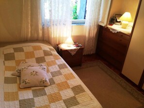 A bedroom with a checkered bedspread, a bedside lamp, a nightstand, and a dresser. - Holiday Home With Parking and 2 Rooms (Dubrovnik)