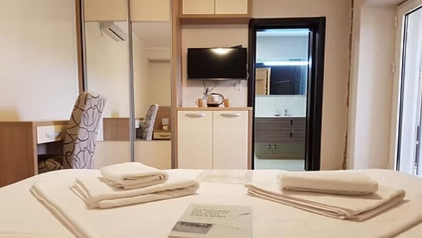 A hotel room with a bed, a flat-screen TV mounted on the wall, a mirror, and a door leading to a bathroom. - Residence Maša- Standard Double Room P7 (Budva)