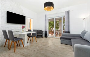 Ein modernes Wohnzimmer mit Flachbildfernseher, einem Essbereich mit Stühlen und Tisch, einer Couch und einer Glastür zum Außenbereich.