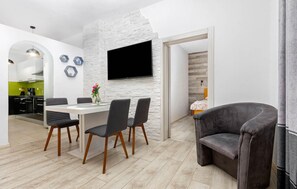 Een moderne woonruimte met een eethoek, een flatscreen televisie bevestigd aan een witte baksteenmuur, en een gezellige zithoek met een donkere gestoffeerde stoel.