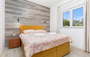 A bedroom with a wooden wall, a bed with a floral bedspread, a nightstand, and a window with a view of trees.