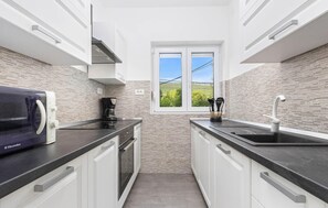 A narrow kitchen with white cabinets, a black countertop, and a window with a view of greenery.