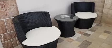 A corner with two wicker chairs and a small round table, likely a seating area in a hotel or similar establishment.