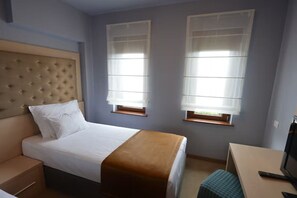 Ett hotellrum med en säng, ett skrivbord, en tv och två fönster med persienner.