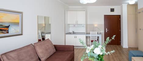 A modern apartment with a brown sofa, a dining table, a kitchen with white cabinets, and a wooden door.