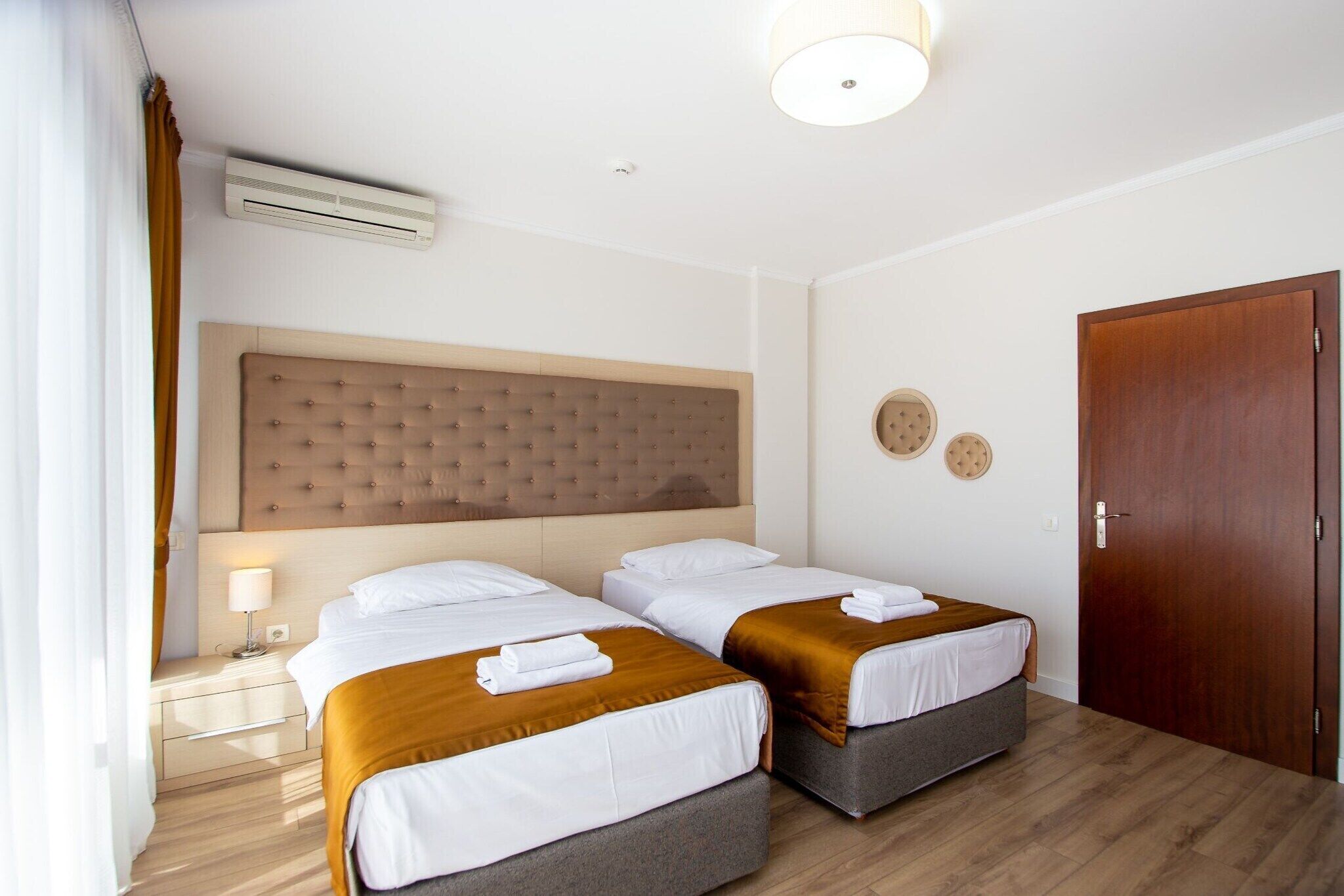 Une chambre d’hôtel avec deux lits, une tête de lit en bois, une table de chevet avec une lampe et une porte.