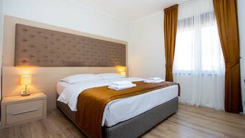 A hotel room with a large bed, a nightstand, a lamp, and a window with curtains.