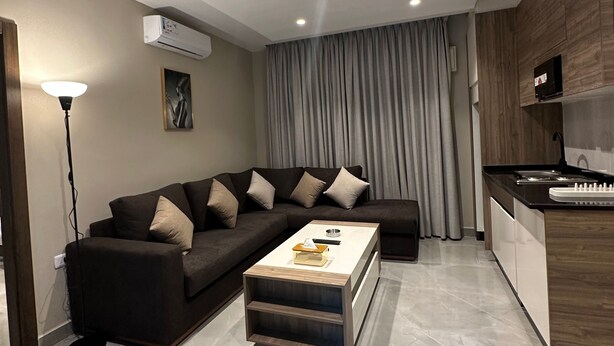 Una sala de estar moderna con un sofá, una mesa de centro y una zona de cocina con mostrador y electrodomésticos.