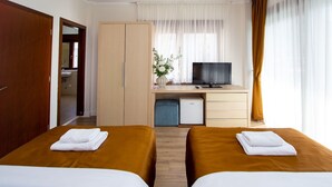 A hotel room with two beds, a desk with a TV, a minibar, and a bathroom visible through an open door. - Hotel Princ- Standard Twin Room 305 (Budva)