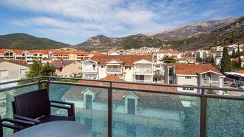 A balcony with a view of a coastal town, featuring terraced houses and mountains in the background.
