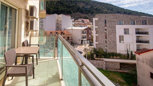 A balcony with a table and chairs, overlooking a residential area with stone buildings and a hilly landscape. - Hotel Princ- Standard Twin Room 305 (Budva)