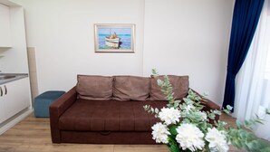 A living room with a brown sofa, a small table, a painting on the wall, and a window with curtains. - Hotel Princ- Standard Twin Room 305 (Budva)