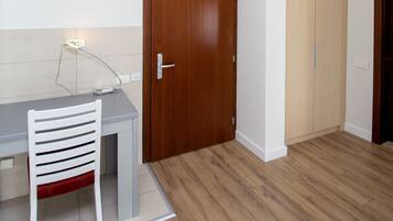 Ein Zimmer mit Holzboden, einem weißen Stuhl, einem grauen Tisch und einer Holztür.