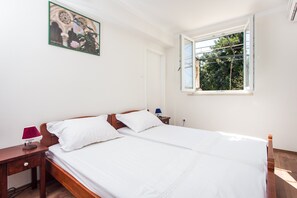 Ein Schlafzimmer mit einem großen Bett, einem Nachttisch, einer Lampe und einem Fenster mit Blick auf Bäume.