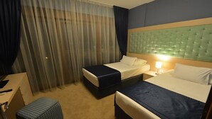 Ett hotellrum med två sängar, ett skrivbord, en stol och ett fönster med gardiner.
