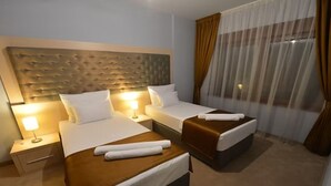 Ett hotellrum med två sängar, en sänggavel, sänglampor och ett fönster med gardiner.