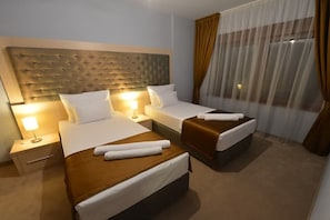 Ein Hotelzimmer mit zwei Betten, einem Kopfteil, einem Nachttisch, einer Lampe und einem Fenster mit Vorhängen.